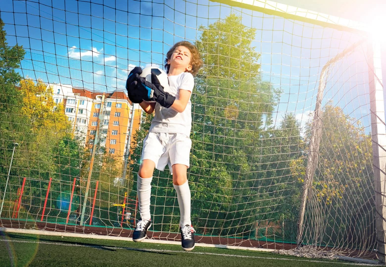 Soccer goalkeeper child in action. Goalkeeper catching the ball. Football soccer game. Boys on the sports field at daytime. Training and practicing.