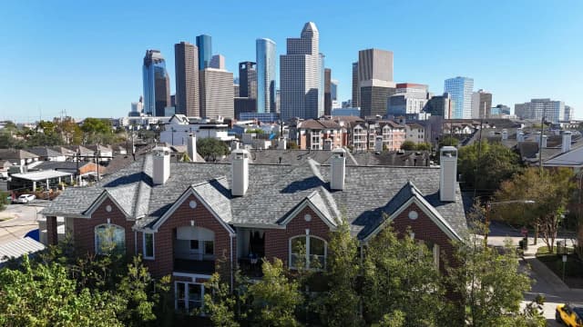 Gray architectural shingles on a brick townhome row, with the Houston skyline behind the roofs.