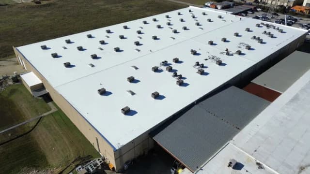 A large commercial building with a bright white flat roof, vents, and rooftop equipment.