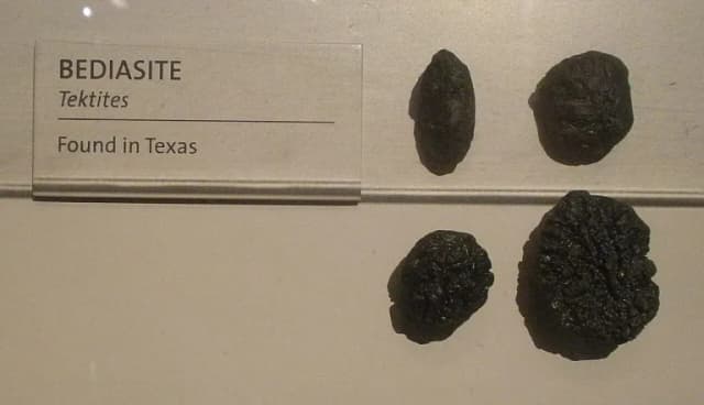 Four dark bediasite specimens in a museum case beside a label that reads Bediasite, Tektites, Found in Texas
