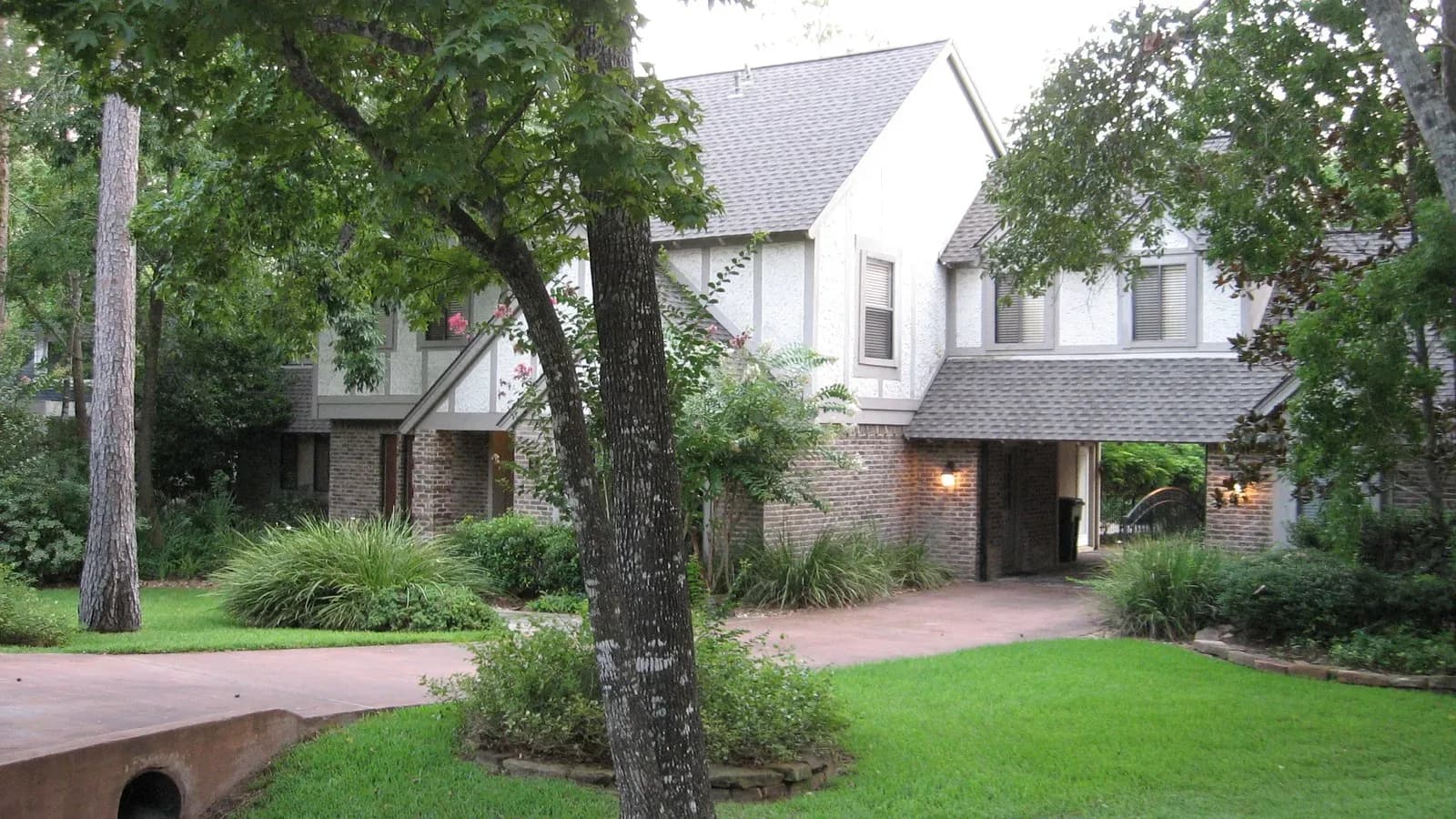 A two-story home behind large shade trees and a green lawn in The Woodlands, Texas
