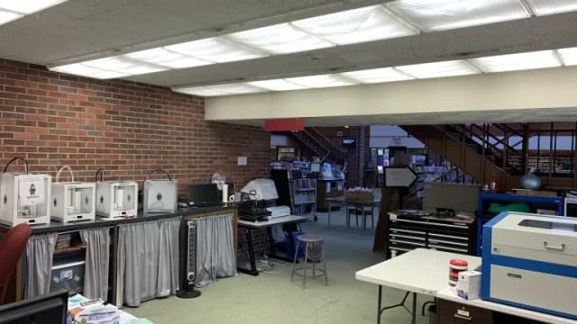 Several 3D printers on a counter in a public library makerspace