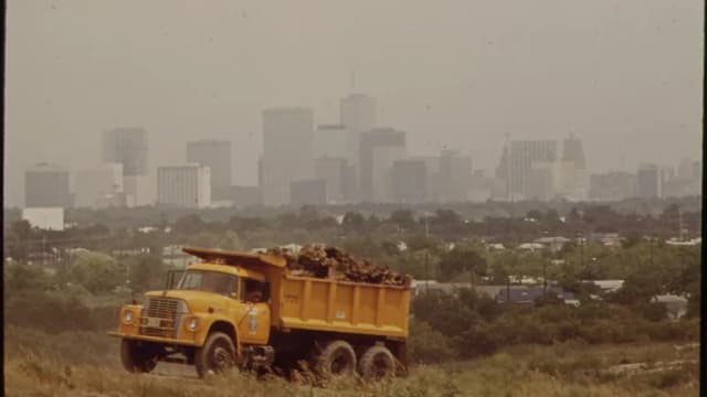 A loaded dump truck on a Houston landfill site in 1972 with the hazy downtown skyline behind it
