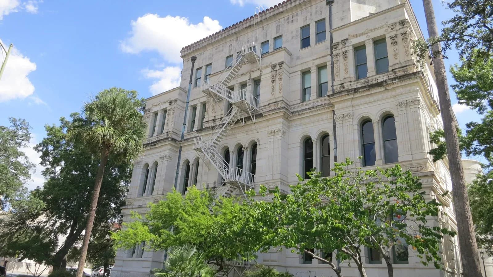 San Antonio City Hall, a stone building with a fire escape, framed by palm and live oak trees