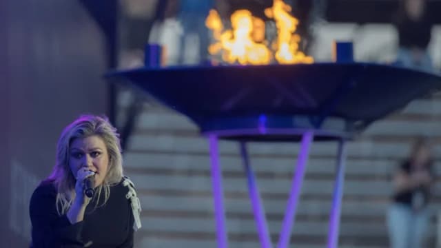 Kelly Clarkson singing into a microphone in front of a lit cauldron