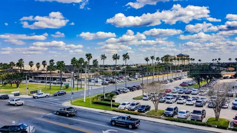 A wide McAllen street lined with palm trees and parking lots under a bright sky
