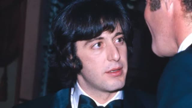 A young Al Pacino in a tuxedo and bow tie speaking with James Caan