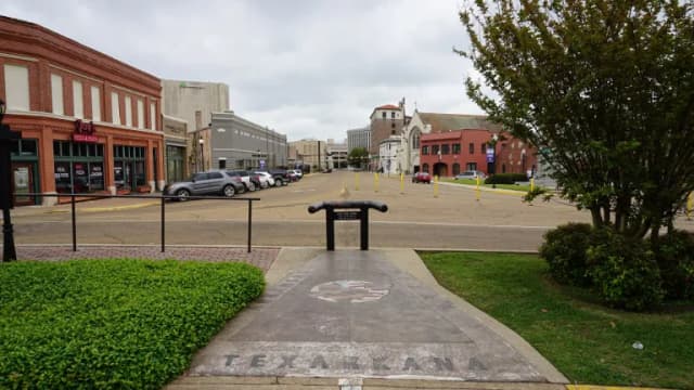 A sidewalk marker reading Texarkana on State Line Avenue, with brick downtown buildings in the background