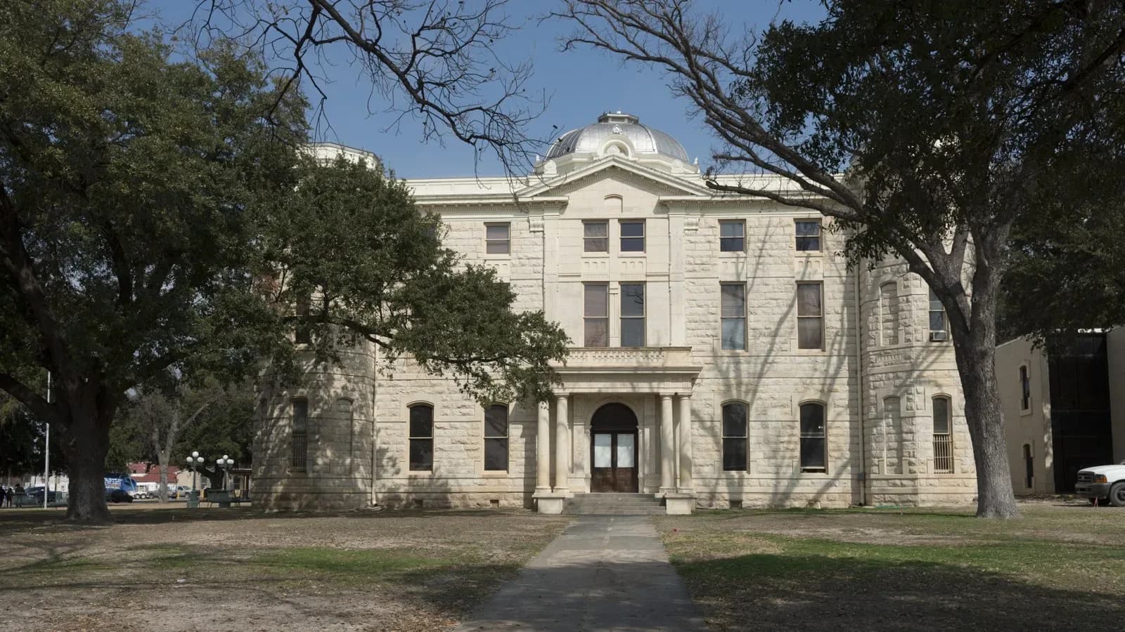 The white limestone Val Verde County Courthouse in Del Rio with a domed cupola, framed by large oak trees