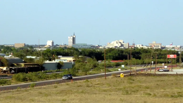 The downtown Odessa skyline seen across open grassland and a road under a clear blue sky