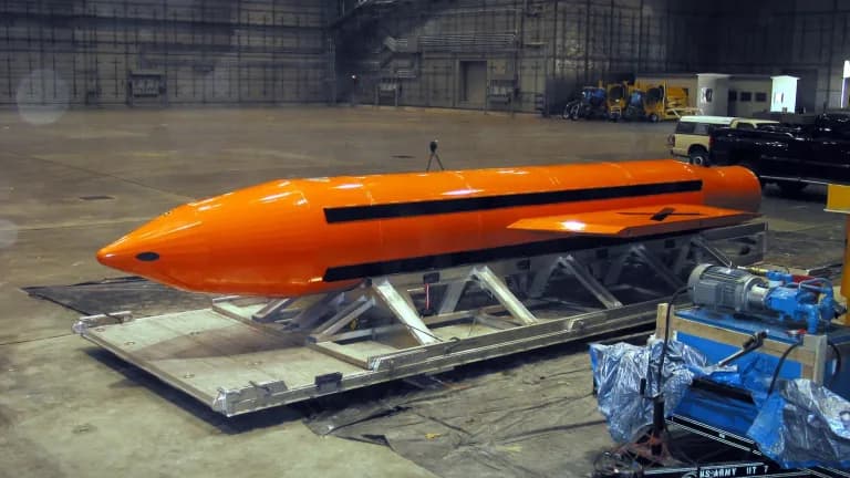 An orange MOAB bomb on a transport cradle inside a hangar