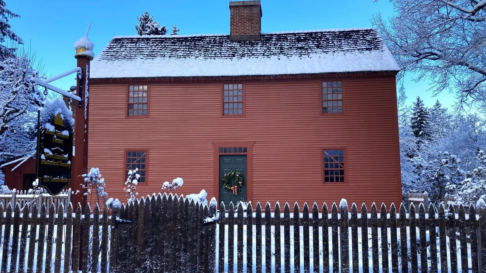 The red colonial Noah Webster House behind a picket fence in snow