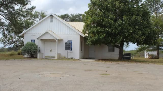Small white rural Baptist church building beside a large shade tree