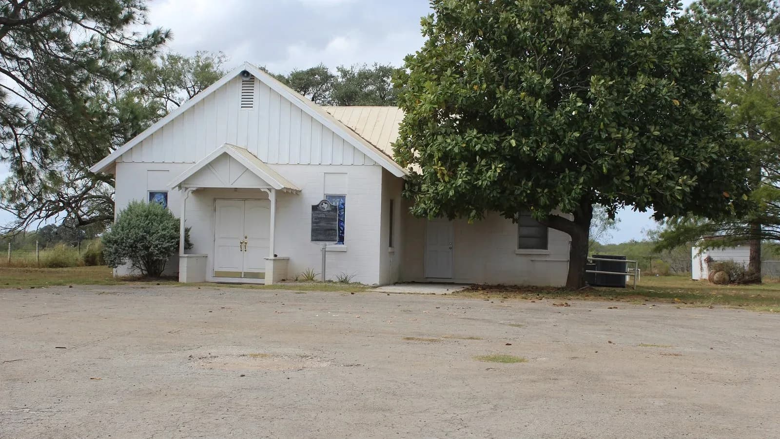 Small white rural Baptist church building beside a large shade tree