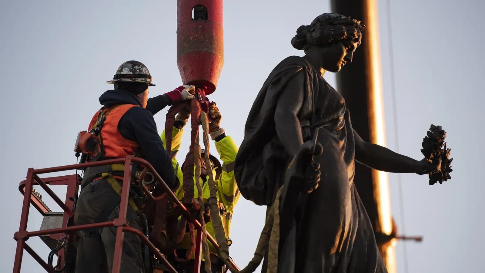 Workers in a lift attach rigging to the bronze figure atop the Confederate Memorial during its removal