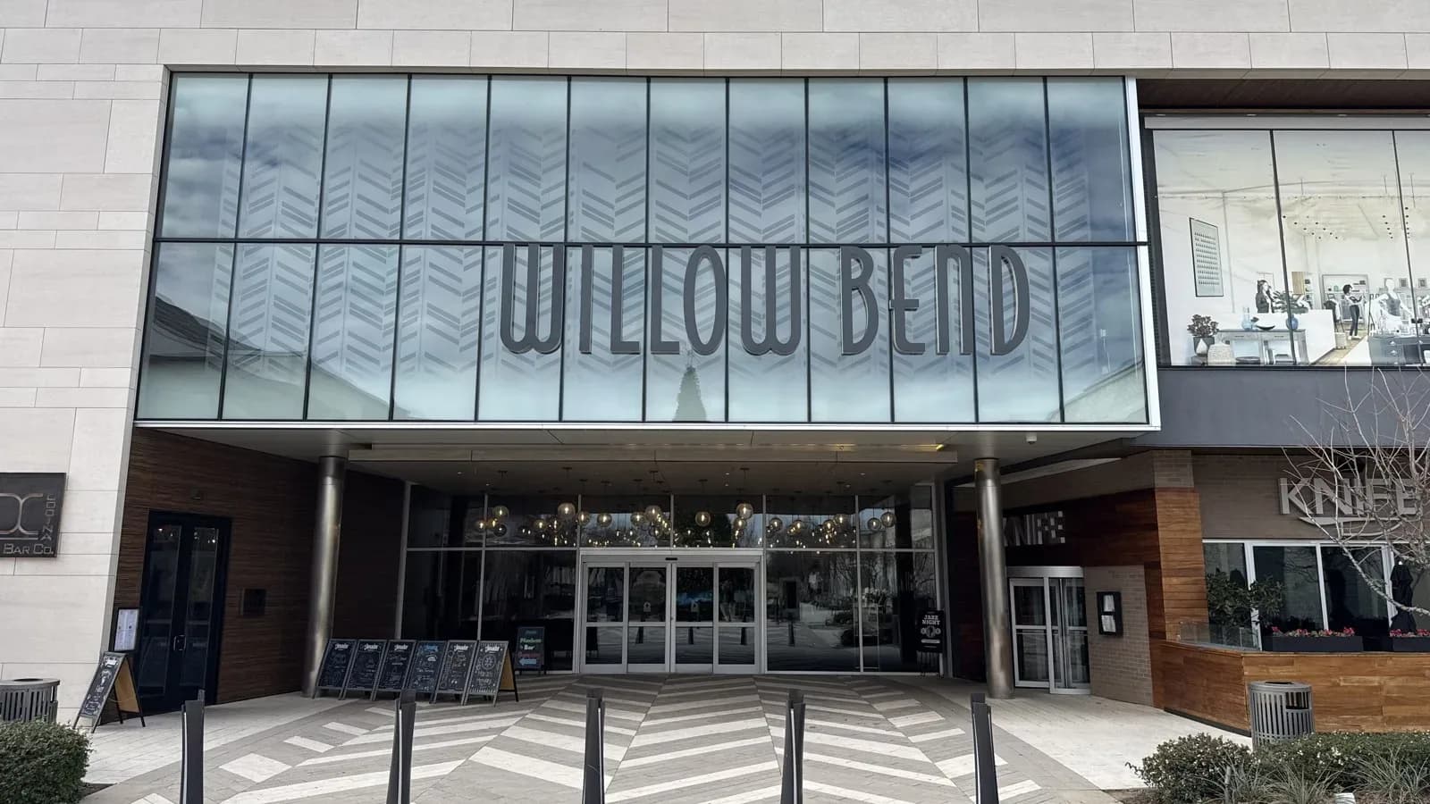 The glass entrance of The Shops at Willow Bend with the mall name in large letters