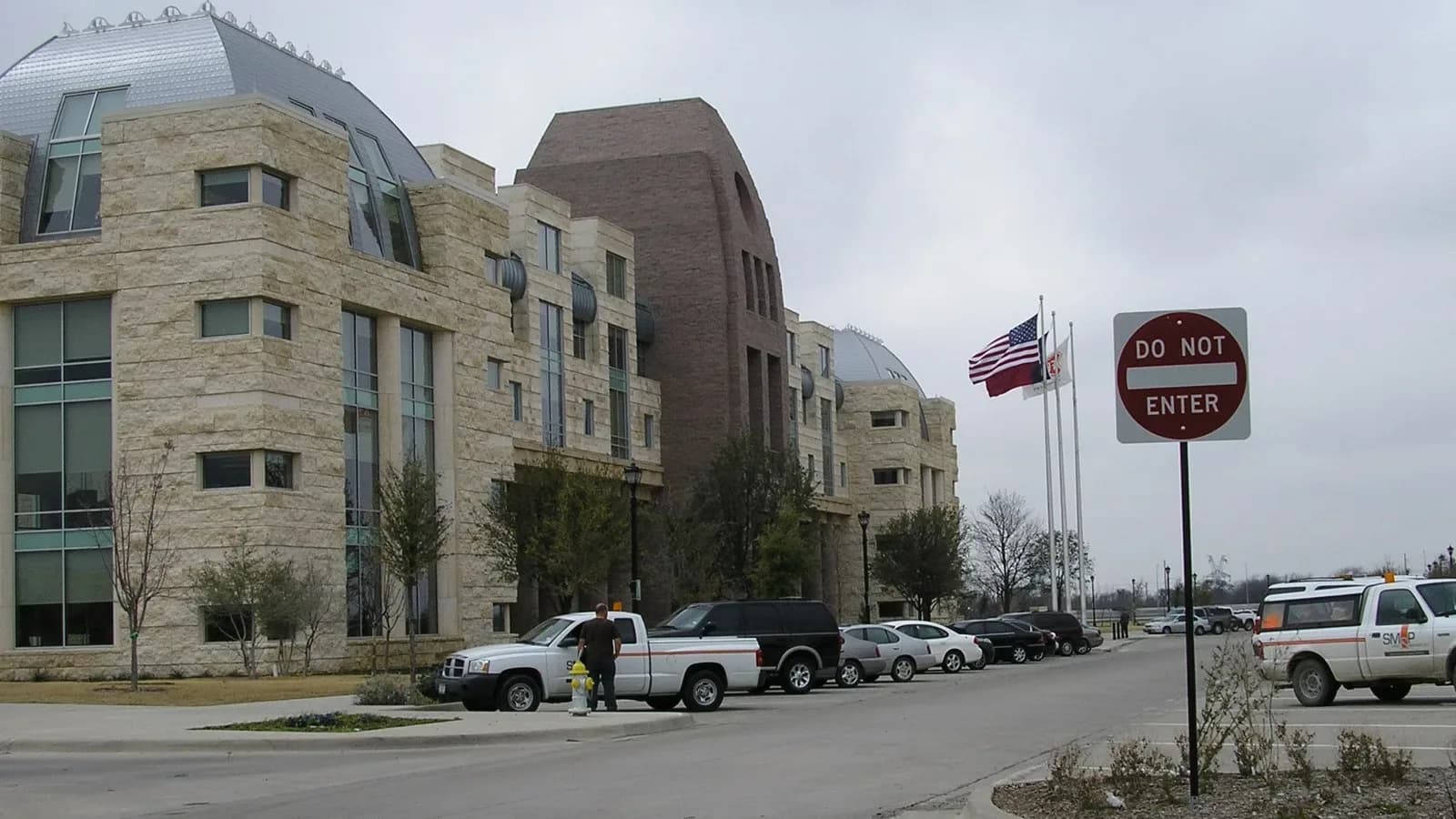 The tan stone Frisco City Hall with domed roofs and flags out front, beside a parking lot
