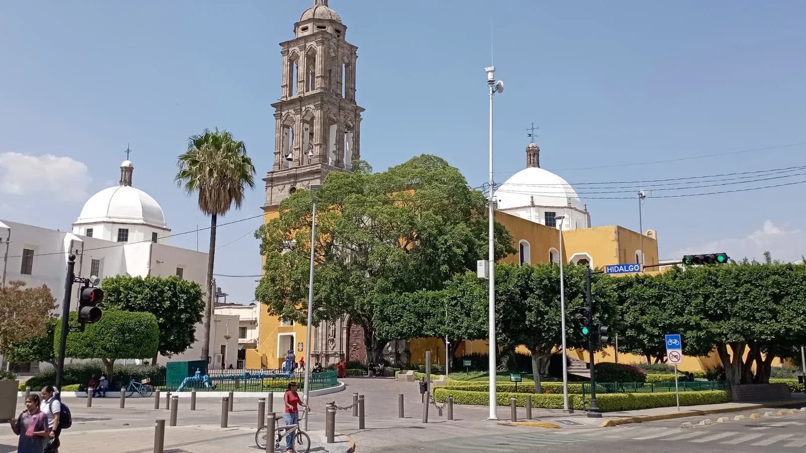 A colonial church bell tower and white domes rise above a tree-lined plaza in Irapuato, Mexico