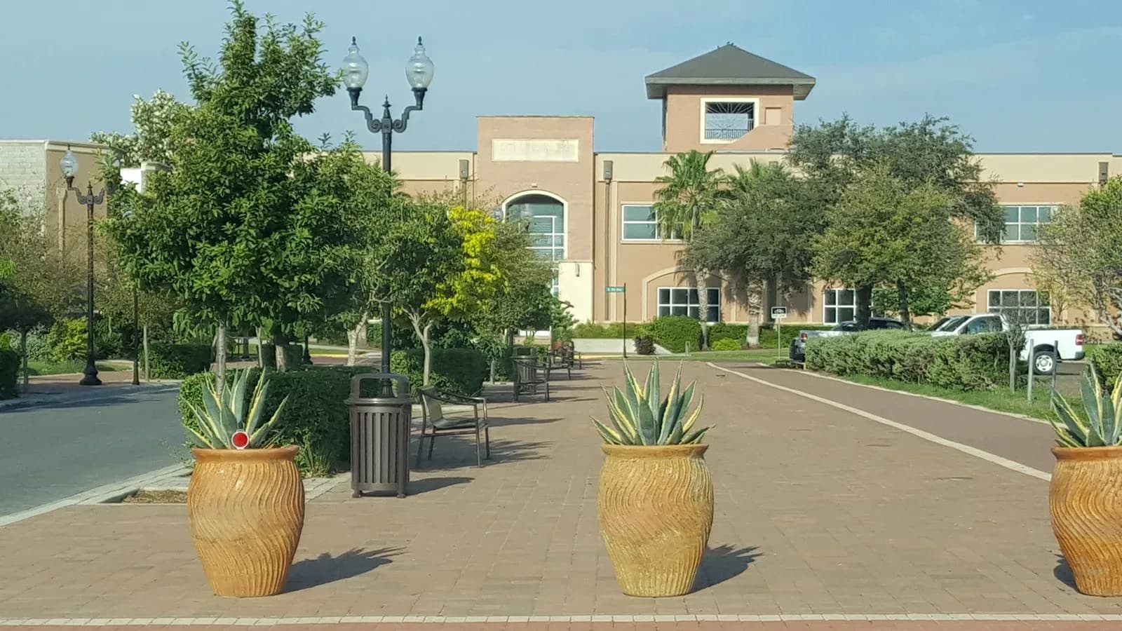 A brick plaza with large potted agave plants leading to Edinburg City Hall under a blue sky
