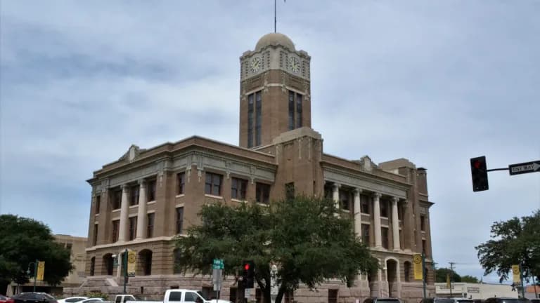 The brick and stone Johnson County Courthouse in Cleburne with its domed clock tower and a flag on top