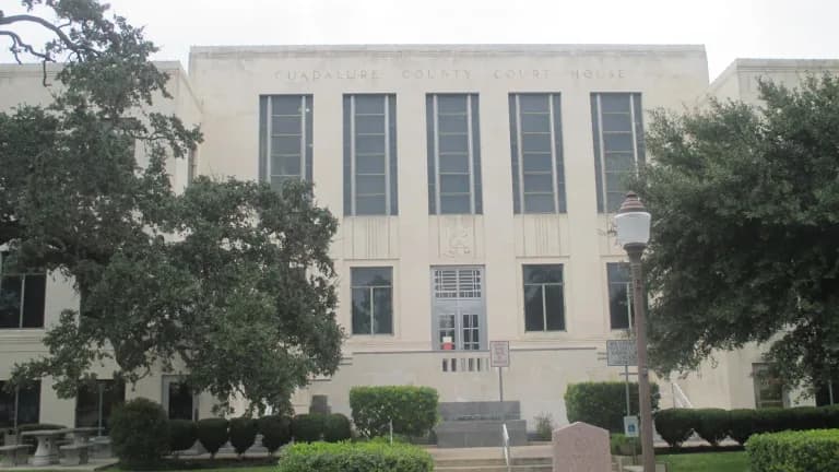 The pale stone Art Deco Guadalupe County Courthouse in Seguin framed by live oaks and trimmed hedges