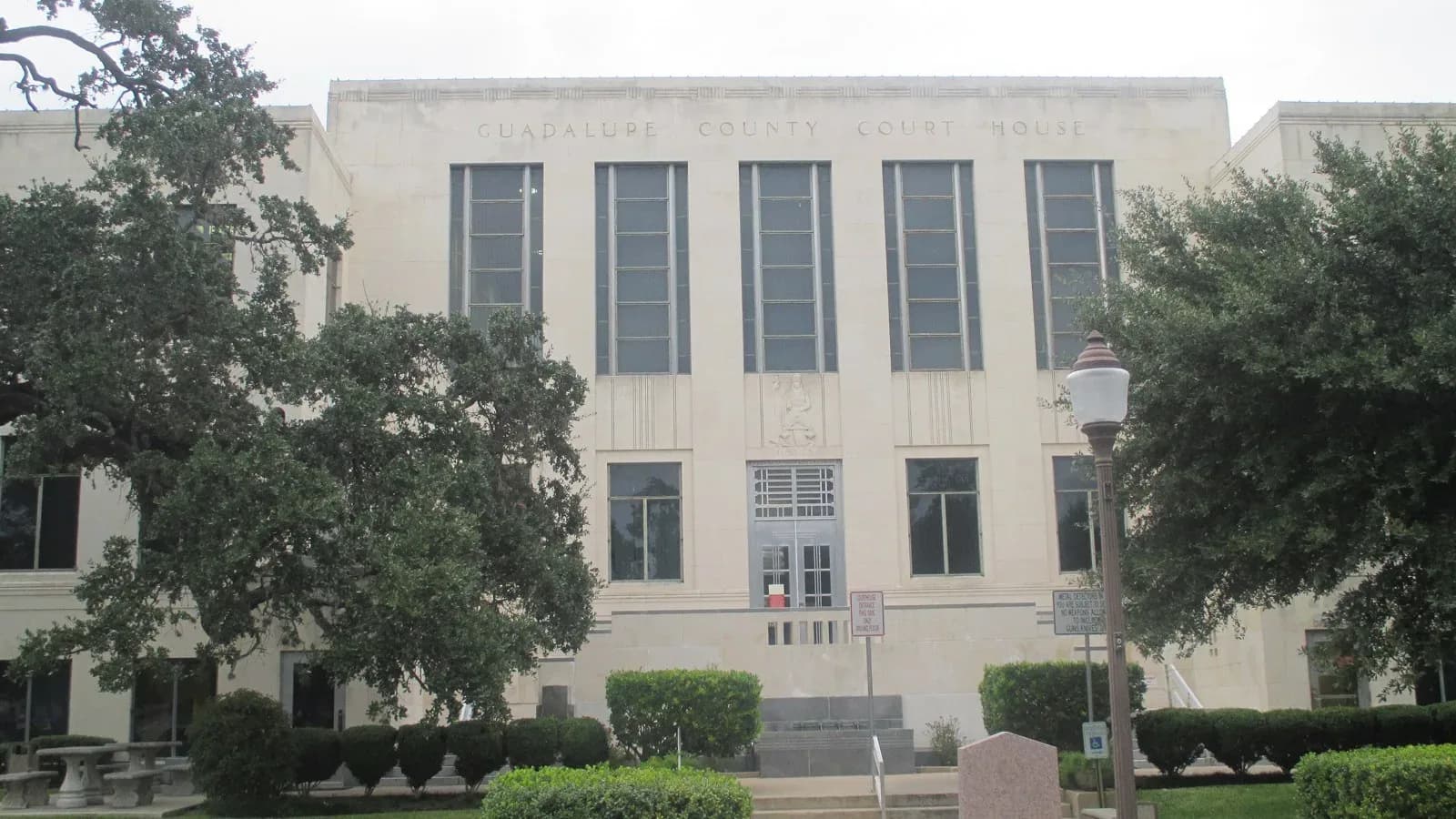 The pale stone Art Deco Guadalupe County Courthouse in Seguin framed by live oaks and trimmed hedges