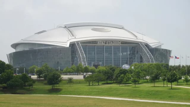 AT&T Stadium in Arlington, a huge glass and steel domed stadium behind a wide green lawn