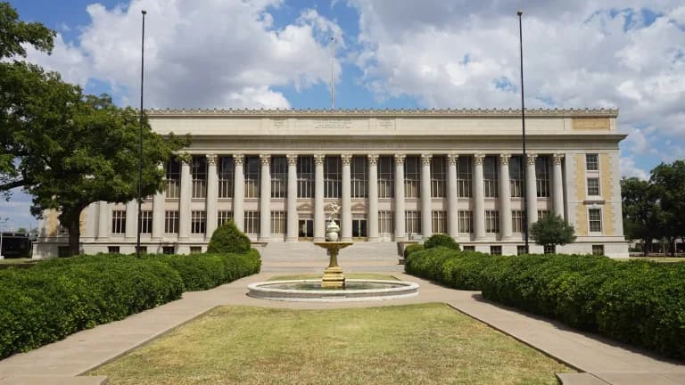 The columned limestone Tom Green County Courthouse in San Angelo behind a fountain and trimmed hedges