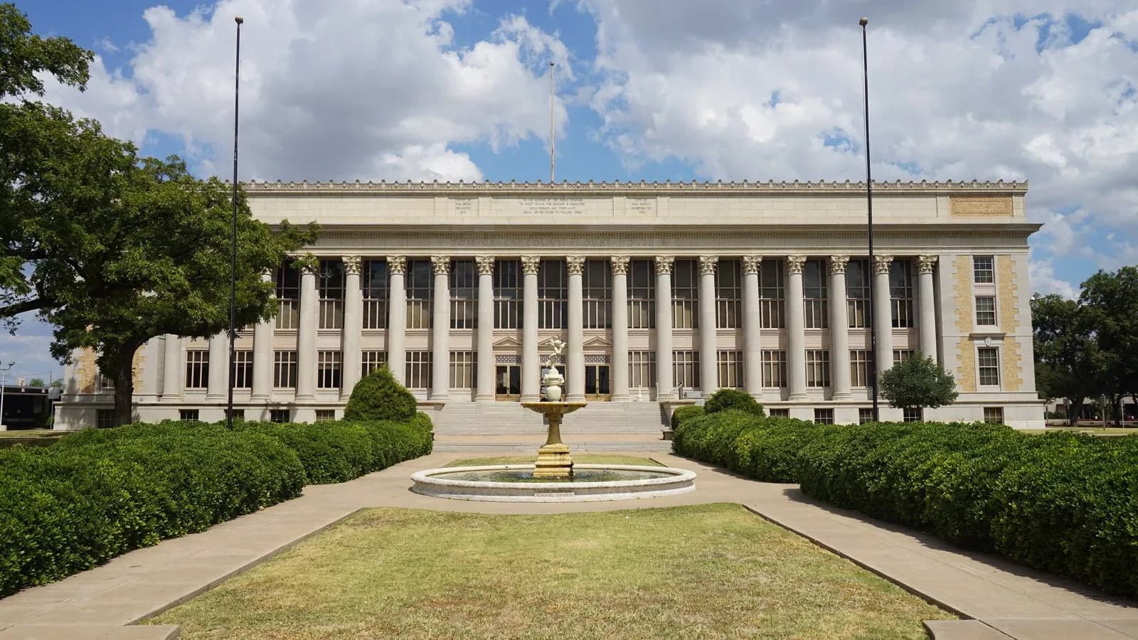 The columned limestone Tom Green County Courthouse in San Angelo behind a fountain and trimmed hedges