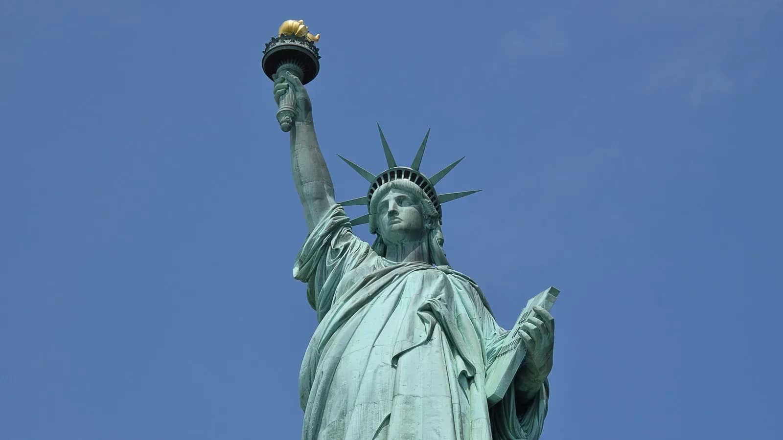 The Statue of Liberty holding her torch aloft against a clear blue sky