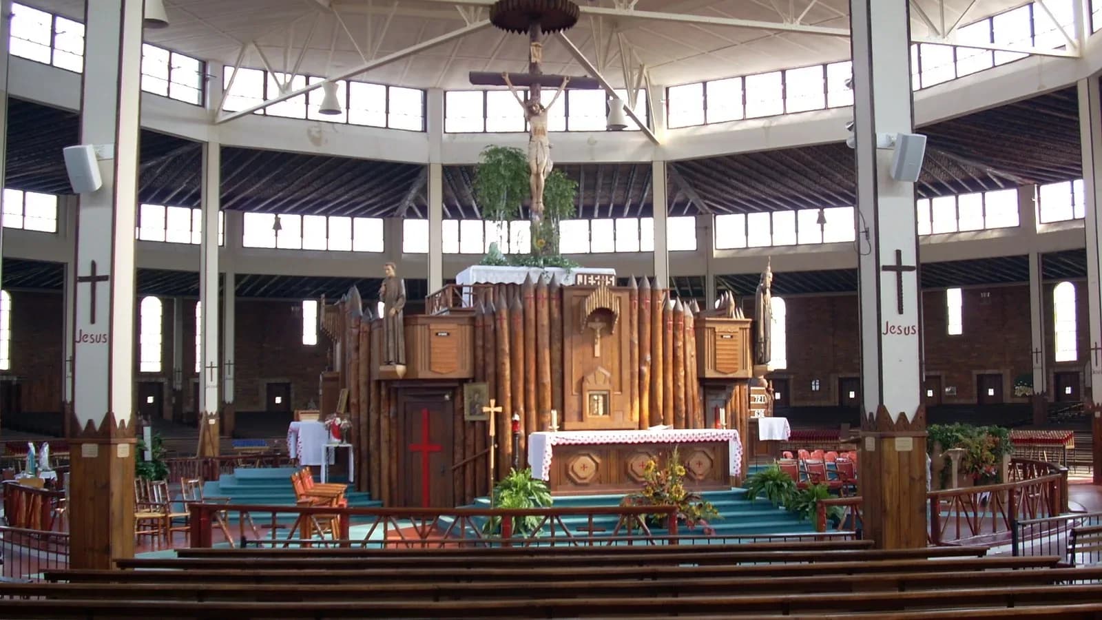 Interior of a large round wooden shrine church with a crucifix hanging above an altar framed by log palisade walls