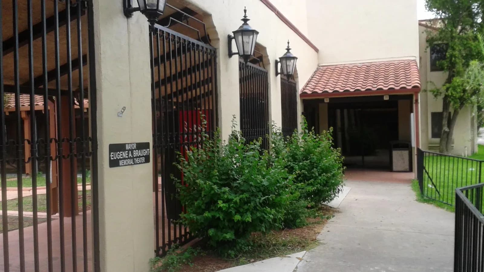 The gated, arched entry to a stucco building with a red tile awning and lantern lights at the Weslaco library