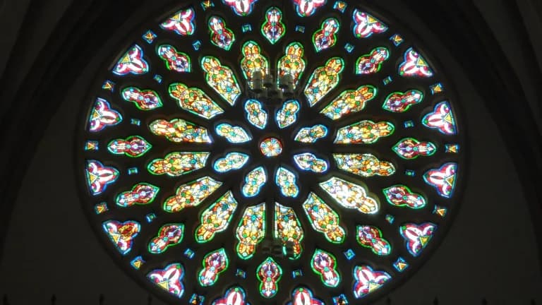 A round stained-glass rose window glowing in red, blue, green and gold inside a dark church
