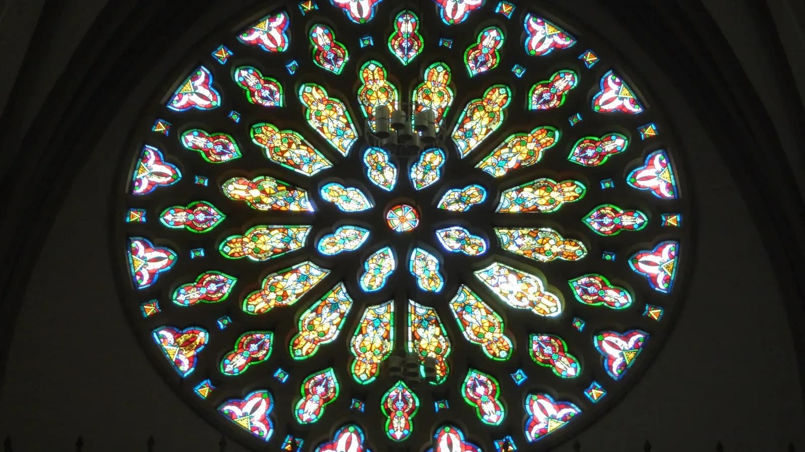 A round stained-glass rose window glowing in red, blue, green and gold inside a dark church