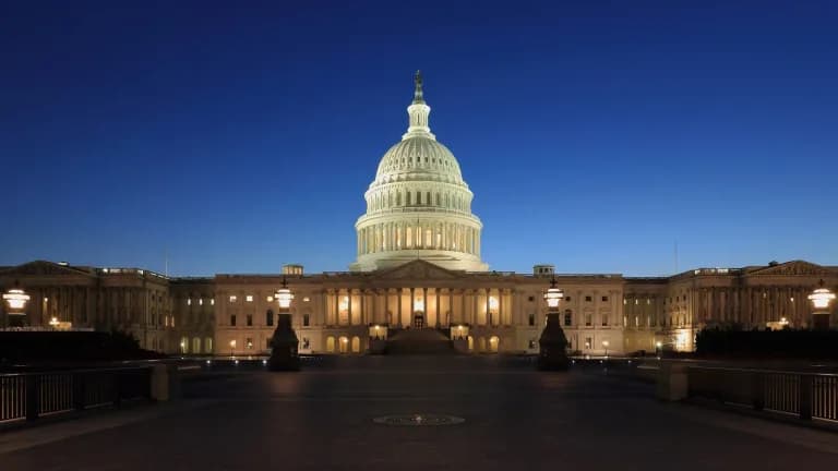 The U.S. Capitol dome lit up at dusk against a deep blue sky, seen from the empty east plaza