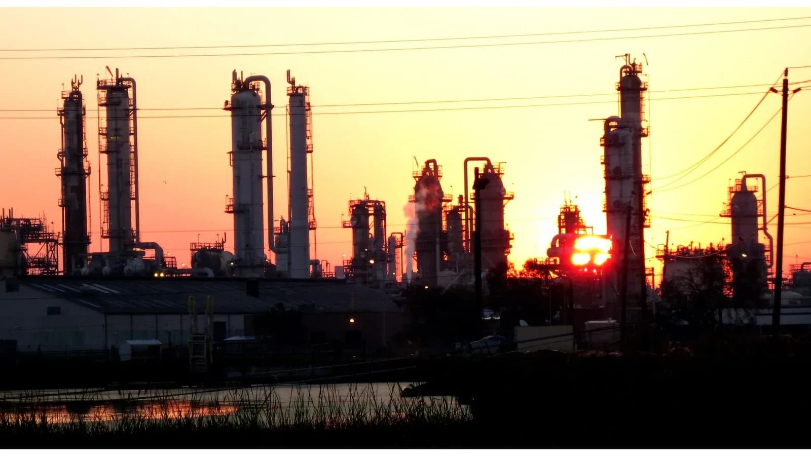 The silhouette of a chemical plant on the Houston Ship Channel against an orange sunrise