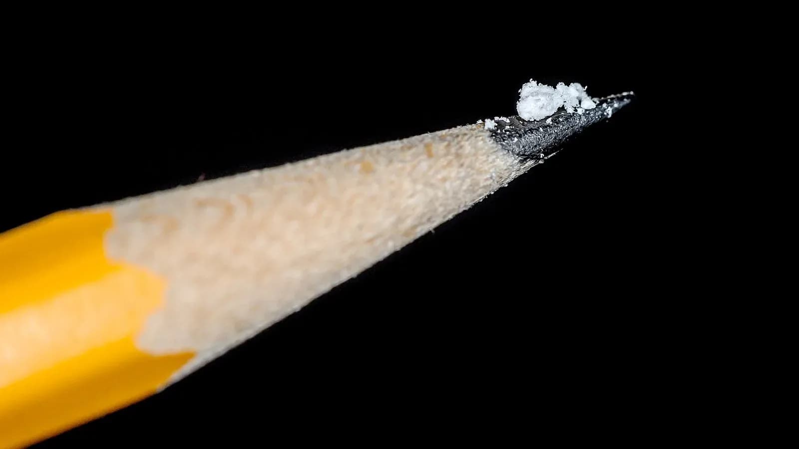 A tiny pile of white powder on the sharpened tip of a yellow pencil against a black background