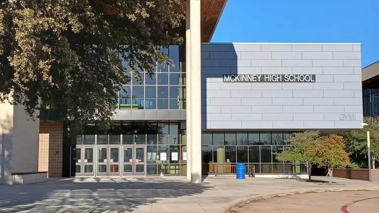 The glass and gray stone entrance of McKinney High School under a blue sky