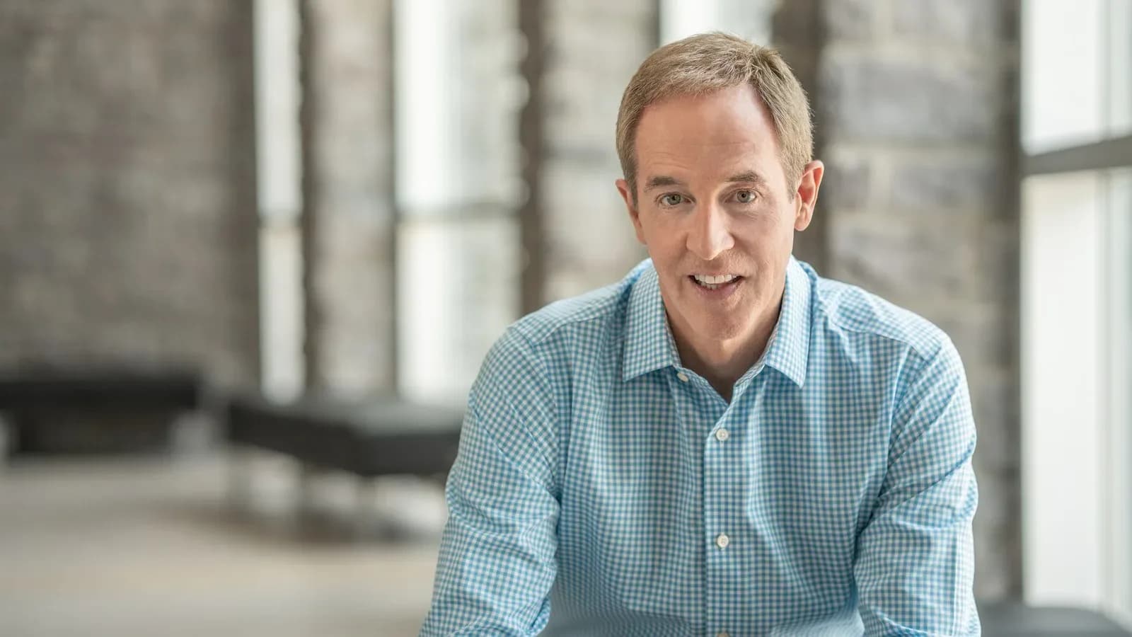 Andy Stanley in a blue checked shirt smiling and speaking in a room with stone walls and tall windows
