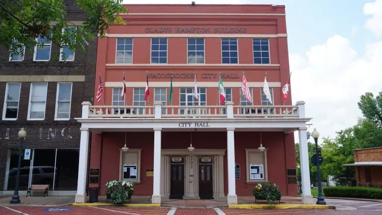 The red-brick Nacogdoches City Hall with a white columned balcony and a row of flags