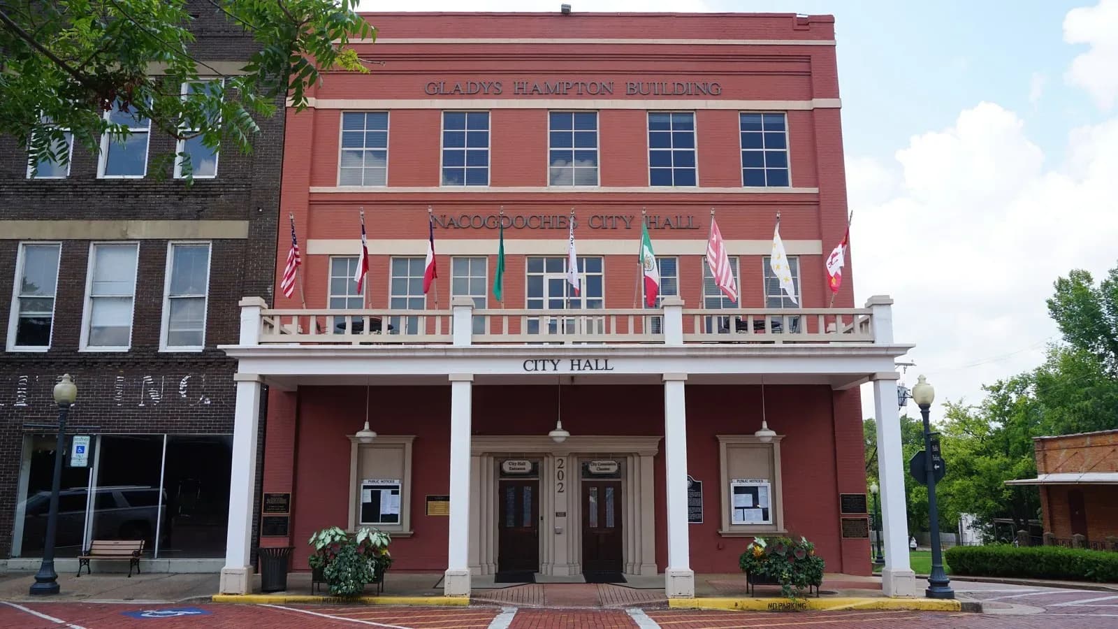 The red-brick Nacogdoches City Hall with a white columned balcony and a row of flags