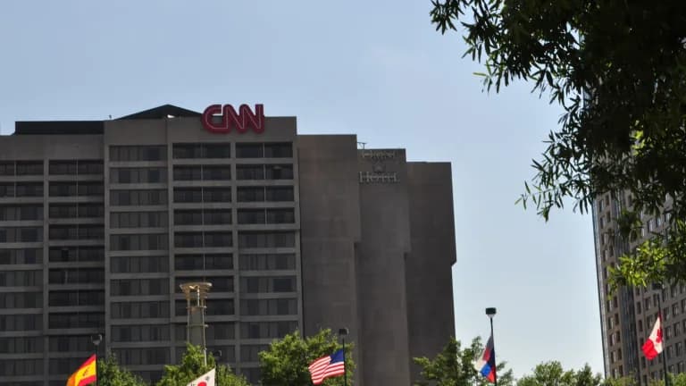 The red CNN letters atop the CNN Center building in downtown Atlanta under a clear sky, with flags and trees in the foreground