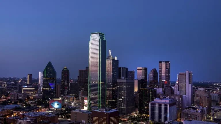 Downtown Dallas skyline at dusk with lighted office towers under a blue evening sky