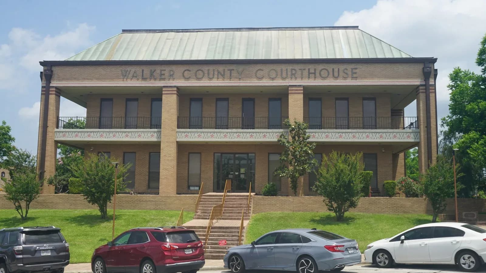 The two-story Walker County Courthouse in Huntsville, Texas, behind a row of parked cars