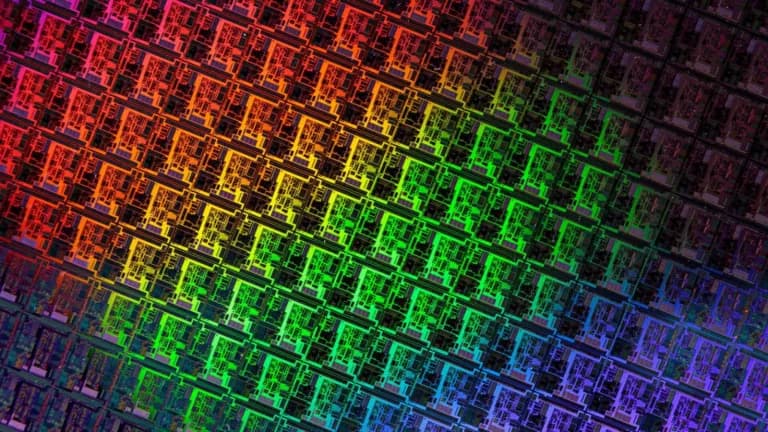 Close-up of a silicon wafer covered in rows of chips reflecting red, green and purple light