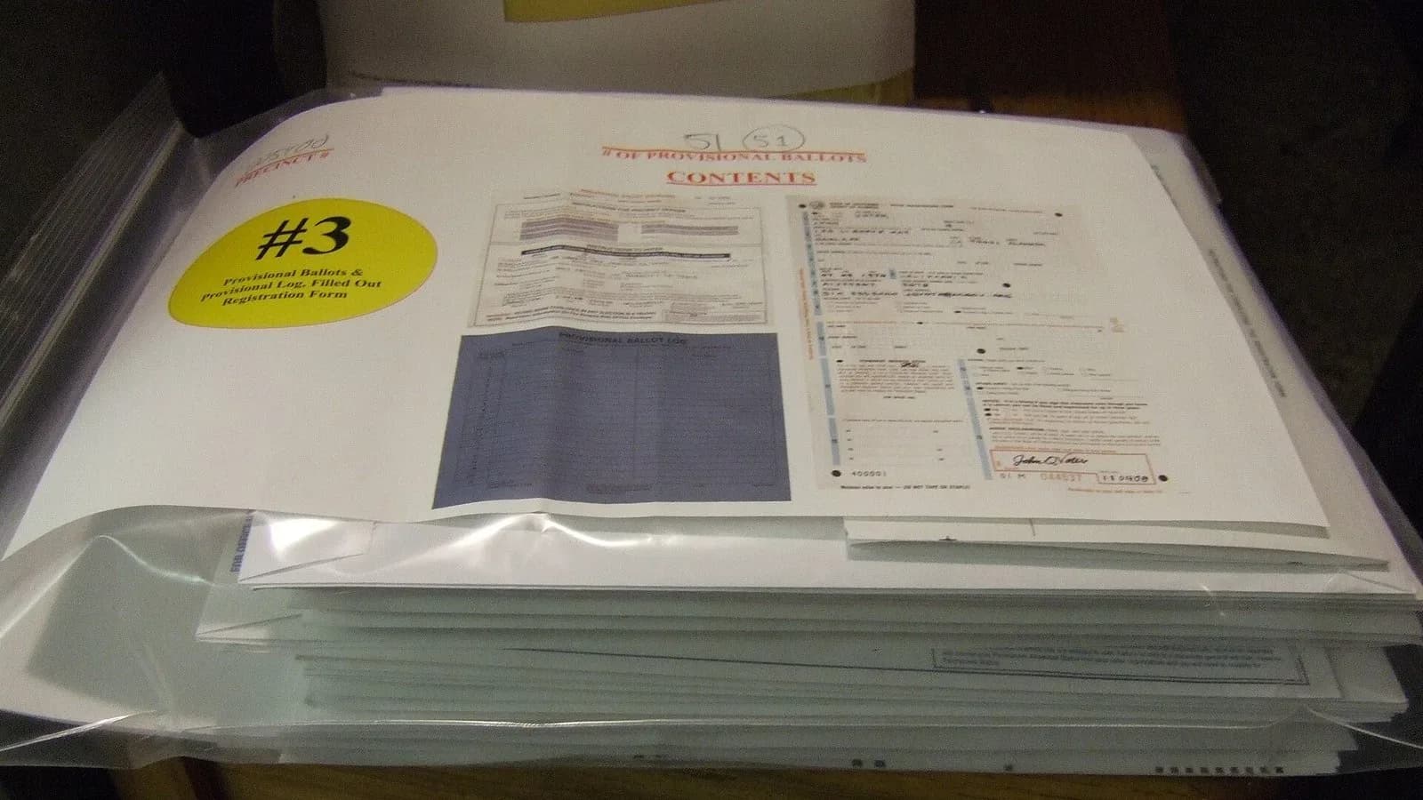A sealed clear plastic bag holding a stack of provisional ballot envelopes and forms on a table