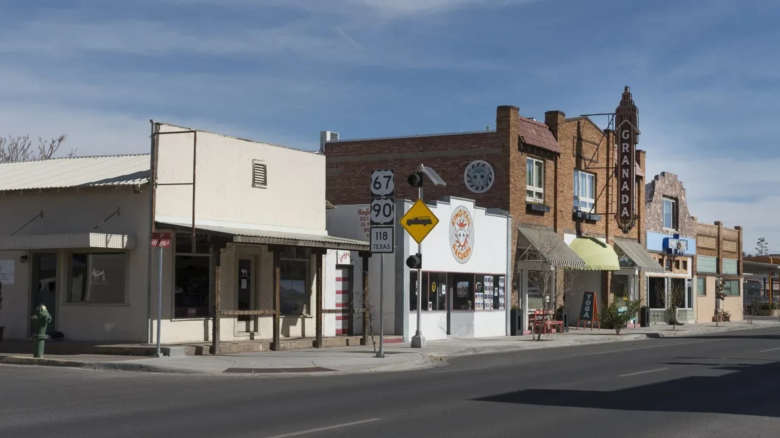 Low storefront buildings and a street corner in downtown Alpine, Texas, under a blue sky