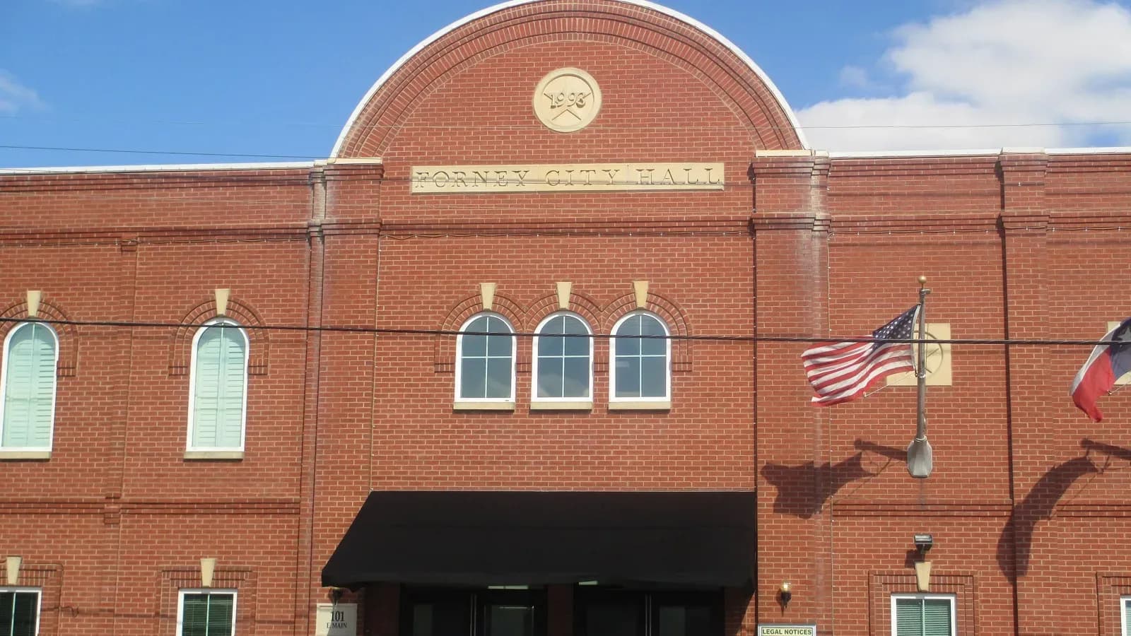 Forney City Hall, a red brick building with an arched gable and American and Texas flags