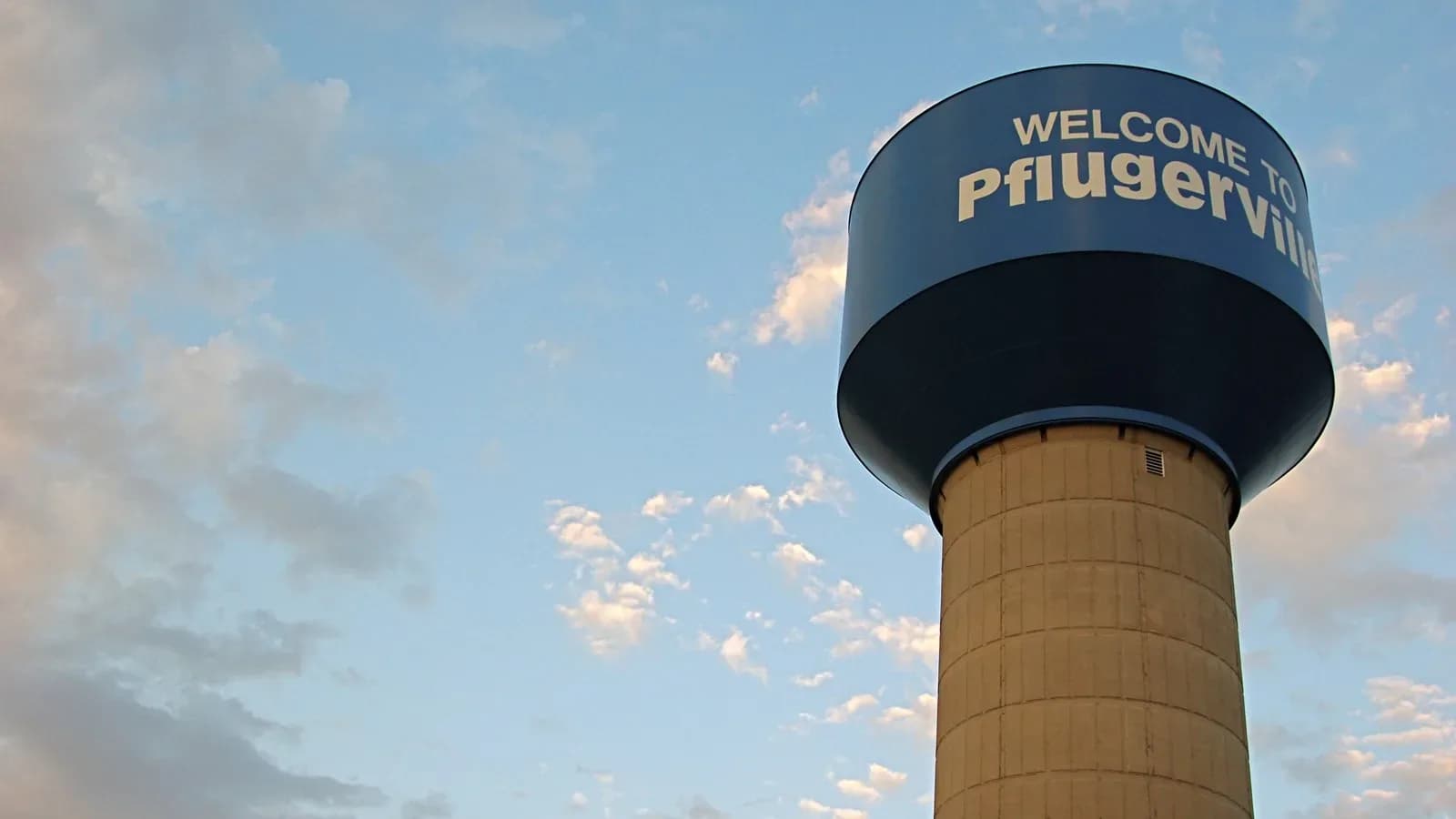 A water tower reading Welcome to Pflugerville against a partly cloudy sky