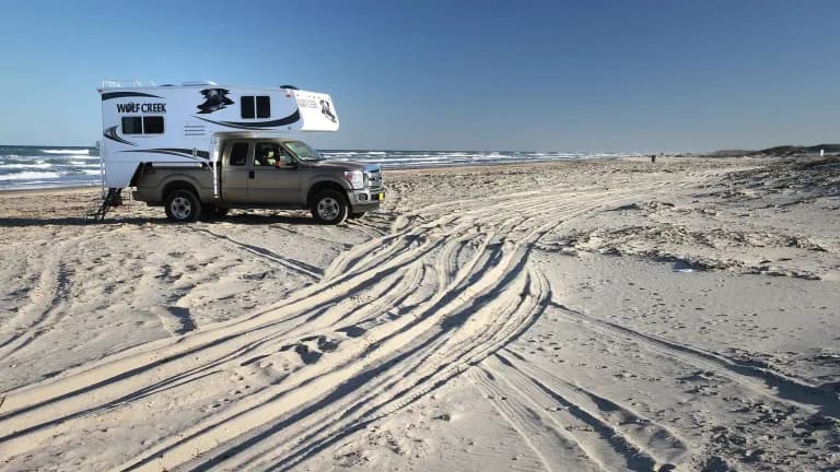 A pickup with a truck camper parked on the sand at Boca Chica Beach as waves roll in
